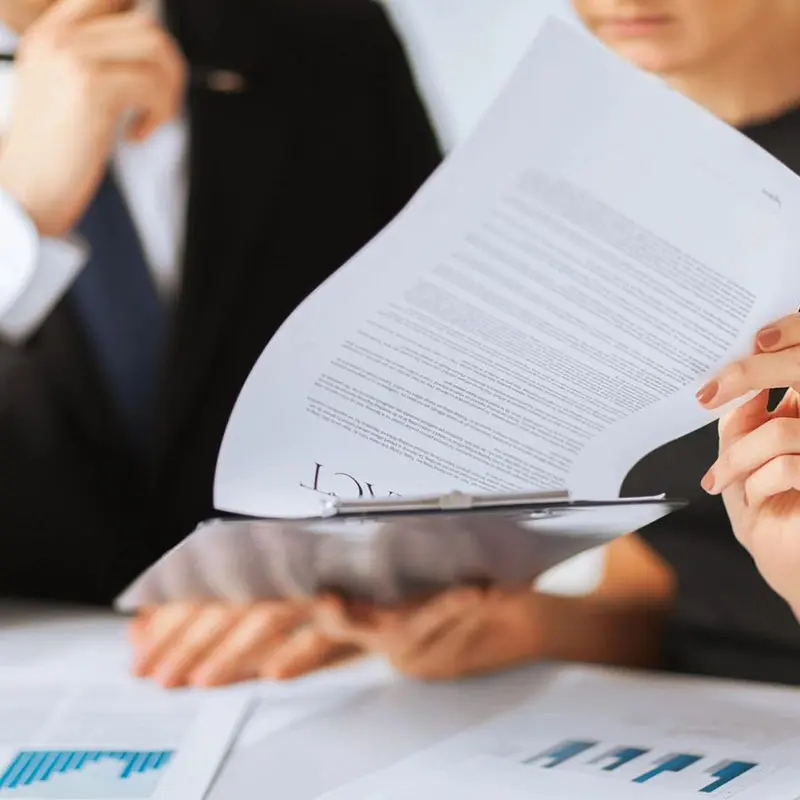 Close-up of three people in formal attire reviewing documents and charts at a meeting.