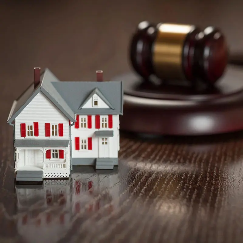 A model house is placed next to a judge's gavel on a wooden table.