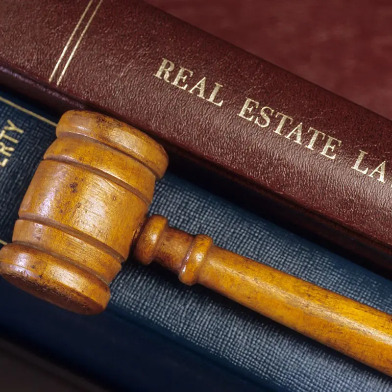 A wooden gavel rests on a stack of legal books, with the top book titled "Real Estate Law.