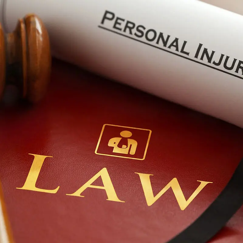 A gavel rests near a rolled document labeled "Personal Injury" atop a red book with the word "Law" in gold letters.